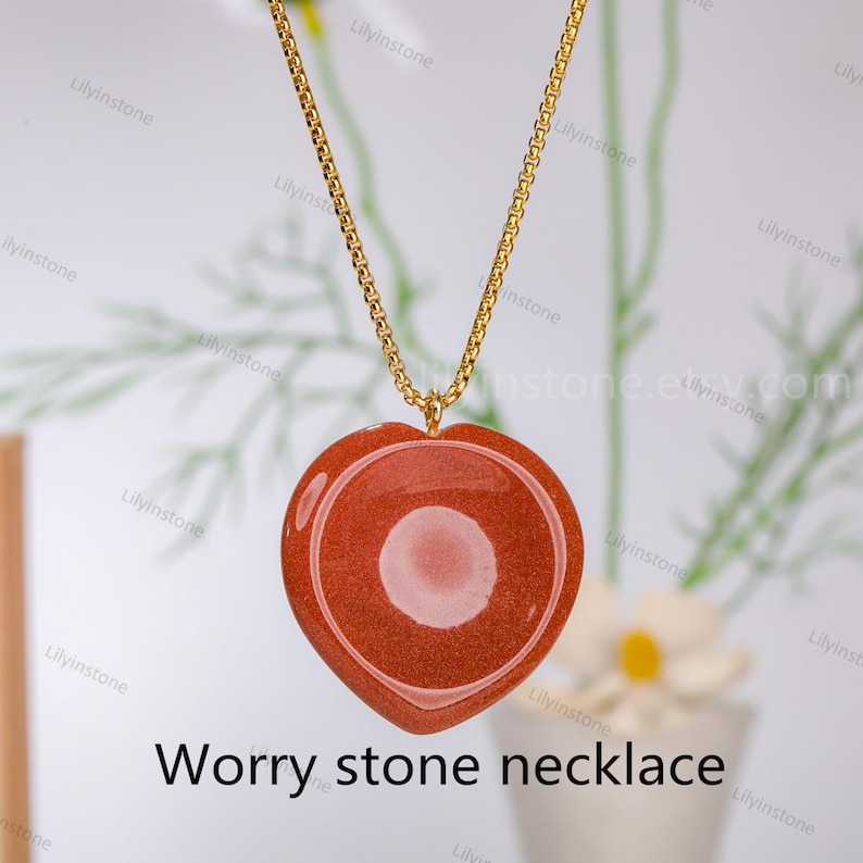 May include: A gold chain necklace with a heart-shaped red worry stone pendant. The stone has a smooth, polished surface.