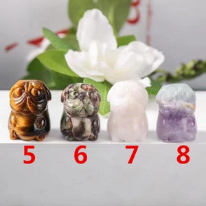 May include: Four small carved pug figurines made of different types of stone. The first is brown and gold tiger's eye, the second is green and brown jasper, the third is white, and the fourth is purple and green fluorite.