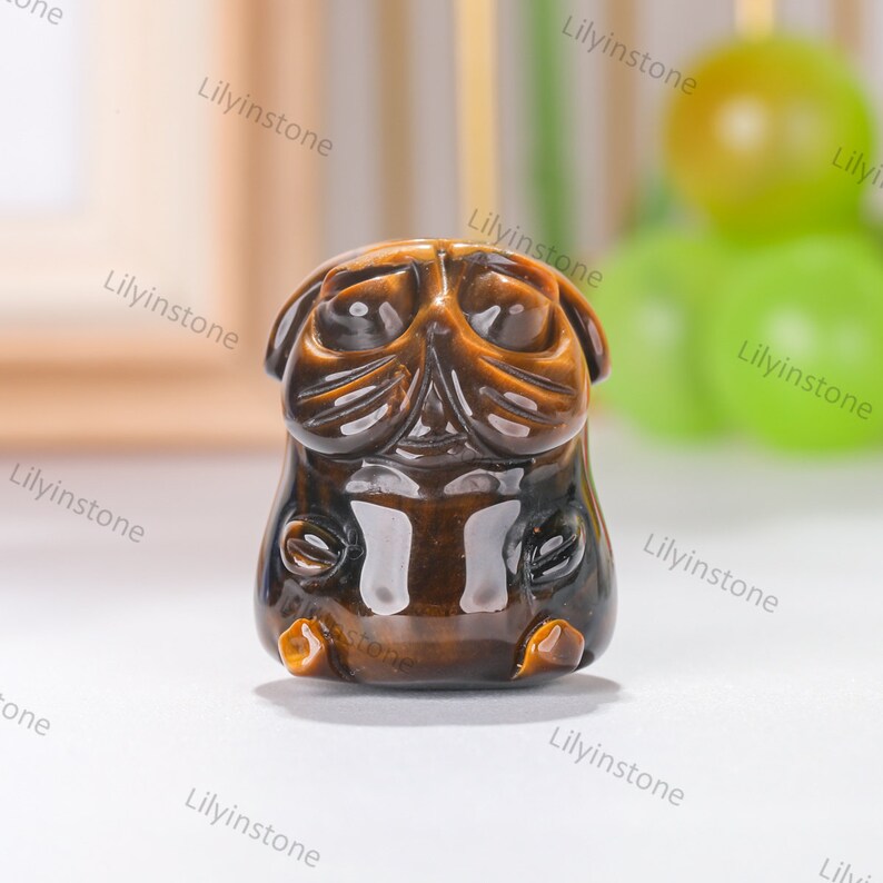 May include: A small, brown, tiger's eye stone carved into the shape of a pug dog. The stone has a shiny, polished finish.