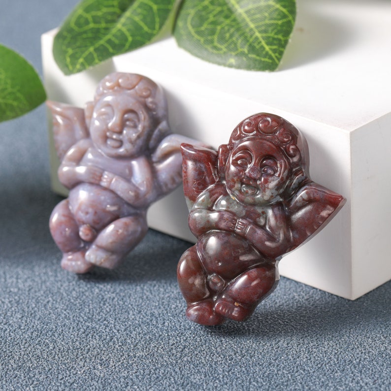 May include: Two carved cherub figurines made of red and purple agate. The cherubs are sitting with their wings spread out.