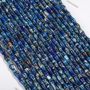 May include: A strand of blue and white patterned, cylindrical beads. The beads are approximately 1.2 cm long and have a smooth, polished finish.