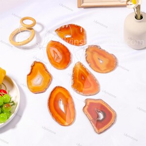 Puede incluir: Un conjunto de siete rodajas de ágata naranja con patrones y texturas naturales, colgando de una cuerda. Las rodajas de ágata están suspendidas sobre un fondo blanco.