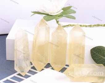 May include: Five yellow citrine crystal points on a white surface. The crystals are smooth and polished, with a slight golden hue.