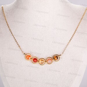 May include: A gold chain necklace with seven round, colorful gemstone beads. The beads are set in gold rings and are arranged in a semi-circle.