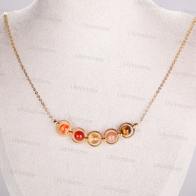 May include: A gold chain necklace with seven round, colorful gemstone beads. The beads are set in gold rings and are arranged in a semi-circle.