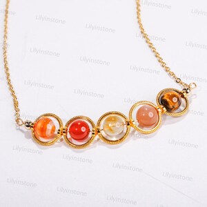 May include: A gold chain necklace with five round gemstone beads in a graduated size. The beads are a mix of orange, red, clear, pink, and brown. The beads are set in gold rings.