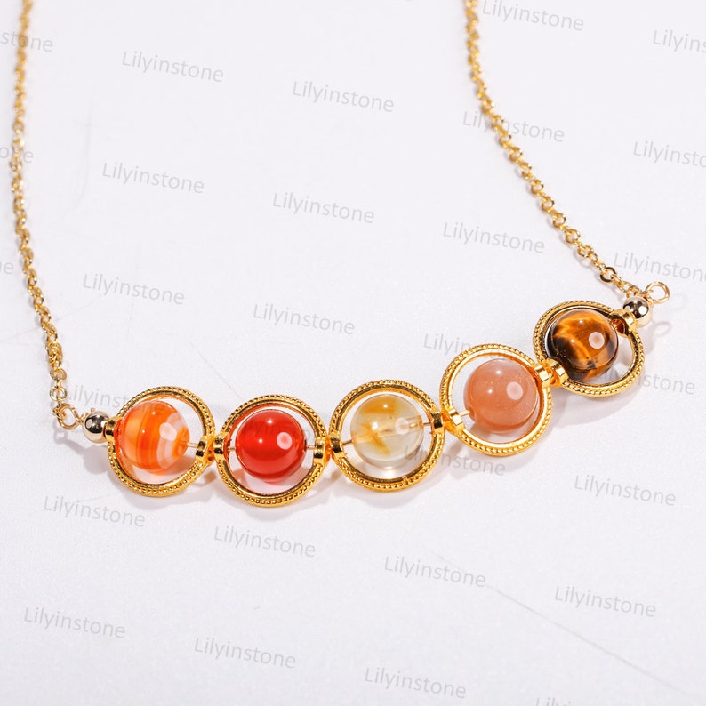 May include: A gold chain necklace with five round gemstone beads in a graduated size. The beads are a mix of orange, red, clear, pink, and brown. The beads are set in gold rings.