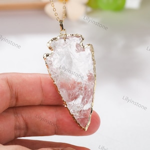 Op de afbeelding: Een hanger in de vorm van een pijlpunt van helder kwarts met een vergulde rand, hangend aan een gouden ketting. De hanger is ongeveer 5 cm lang.