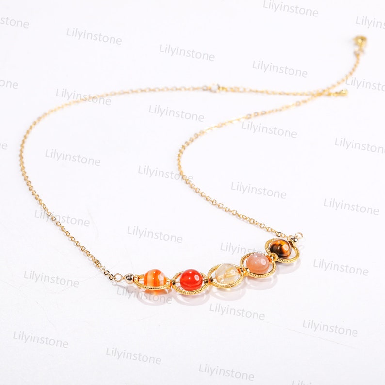 May include: A gold chain necklace with seven colorful gemstone beads. The beads are in a rainbow pattern, starting with red and ending with brown. The necklace is on a white background.
