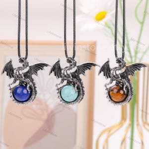 May include: Three silver dragon necklaces with gemstone pendants. The pendants are a blue lapis lazuli, a turquoise, and a tiger's eye.