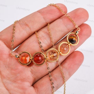May include: A gold chain necklace with five round gemstone beads. The beads are encased in gold rings. The beads are red, orange, yellow, and brown.