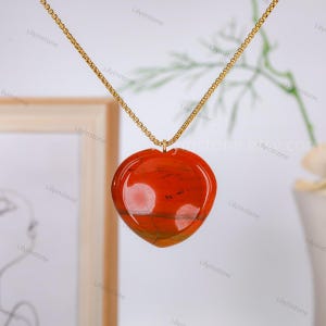 May include: A gold chain necklace with a heart-shaped pendant made of red and orange agate.