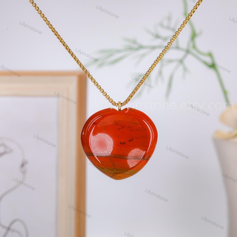 May include: A gold chain necklace with a heart-shaped pendant made of red and orange agate.