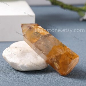 May include: A clear, faceted, golden citrine crystal point with a double termination. The crystal is resting on a white rock.
