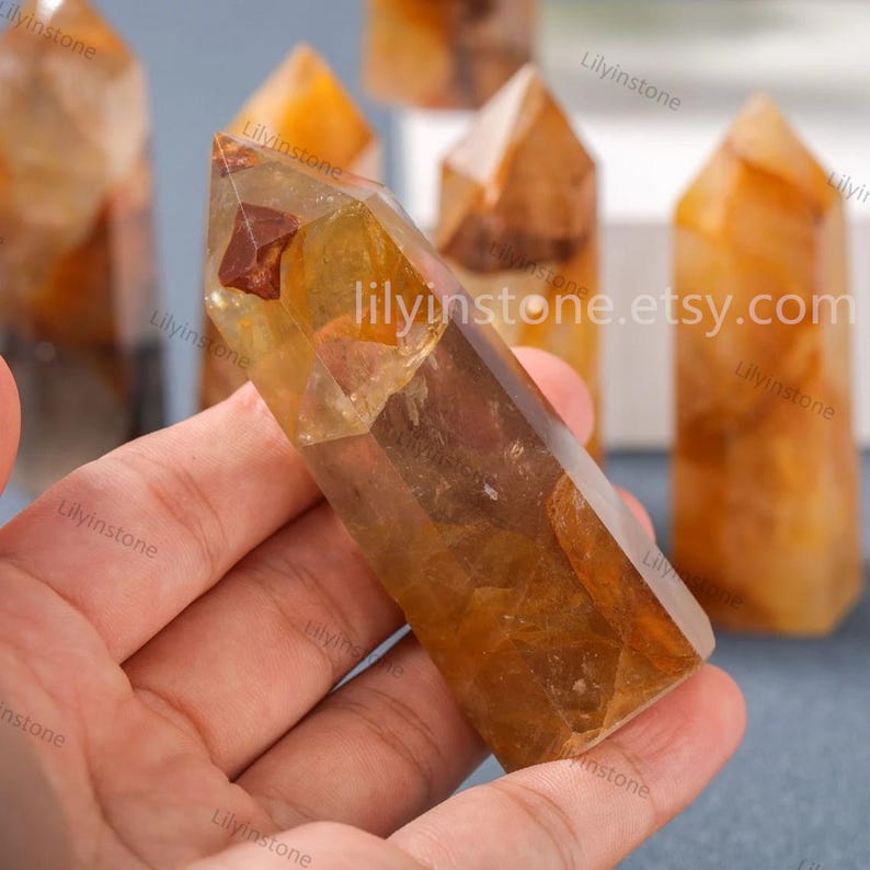 May include: A collection of six golden citrine crystal points, with one point being held in a hand. The points are clear with a golden hue and have a natural, raw finish. The points are all different sizes and shapes. The text "lillyinstone.etsy.com" is visible in the image.