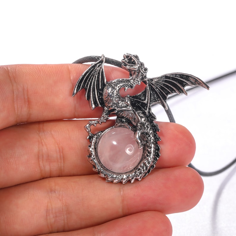 May include: A silver dragon pendant with a pink rose quartz gemstone. The dragon is curled around the stone, with its wings spread out.
