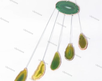 Puede incluir: Un carillón de ágata verde con cinco rodajas de ágata pulidas que cuelgan de un anillo de metal. Las rodajas son de varios tonos de verde y amarillo.