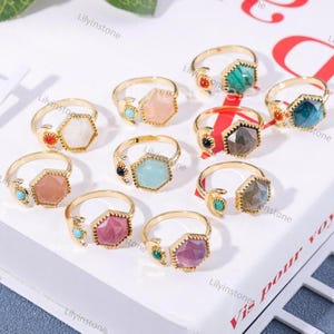 Puede incluir: Surtido de anillos de oro con piedras preciosas de diferentes colores. Cada anillo presenta un diseño de media luna y una piedra preciosa hexagonal. Las piedras preciosas incluyen rosa, blanco, verde, azul y morado.