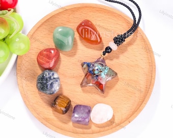 May include: A star-shaped pendant necklace with a variety of colorful stones, including red, green, blue, and brown. The necklace is on a wooden plate with seven tumbled stones in different colors.