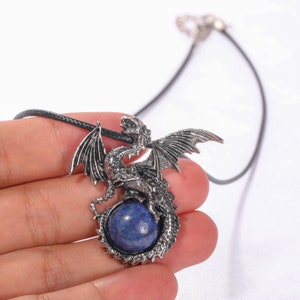 May include: A silver dragon pendant necklace with a blue lapis lazuli gemstone. The dragon is curled around the stone, with its wings spread out.