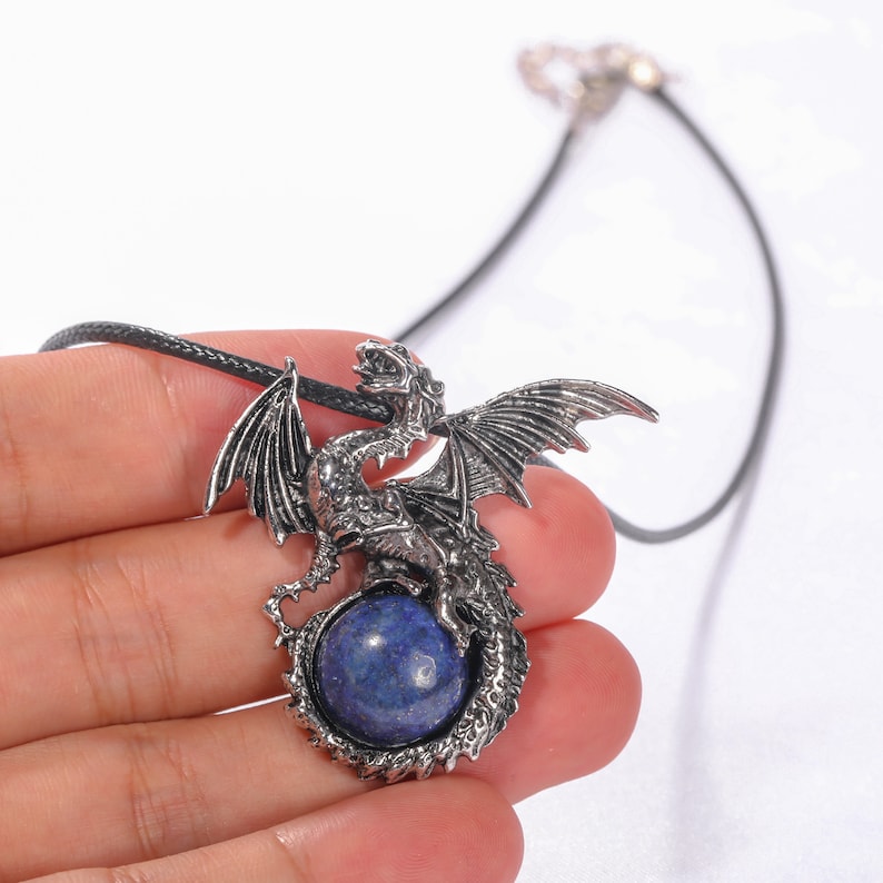 May include: A silver dragon pendant necklace with a blue lapis lazuli gemstone. The dragon is curled around the stone, with its wings spread out.