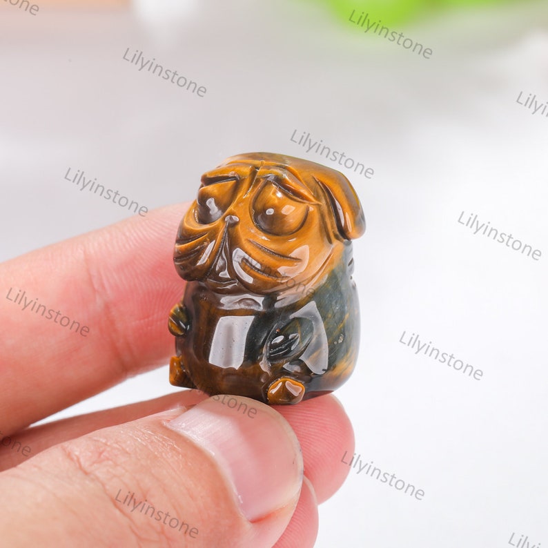 May include: A small, carved pug figurine made of tiger's eye stone. The figurine is brown and gold with a glossy finish.