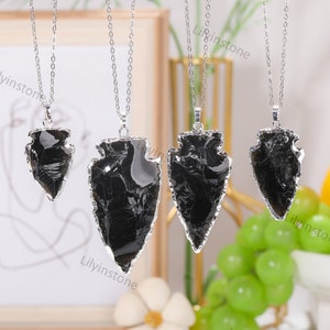 May include: Four silver necklaces with black arrowhead pendants. The arrowheads are made of obsidian and have a natural, rough texture. The necklaces are all of different lengths.