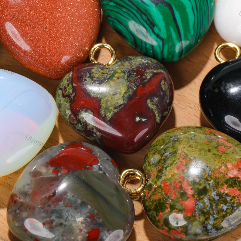 Peut inclure: Assortiment de pierres polies en forme de c&oelig;ur avec des anneaux de saut dor&eacute;s. Les pierres sont de diff&eacute;rentes couleurs, notamment rouge, vert, noir et blanc.