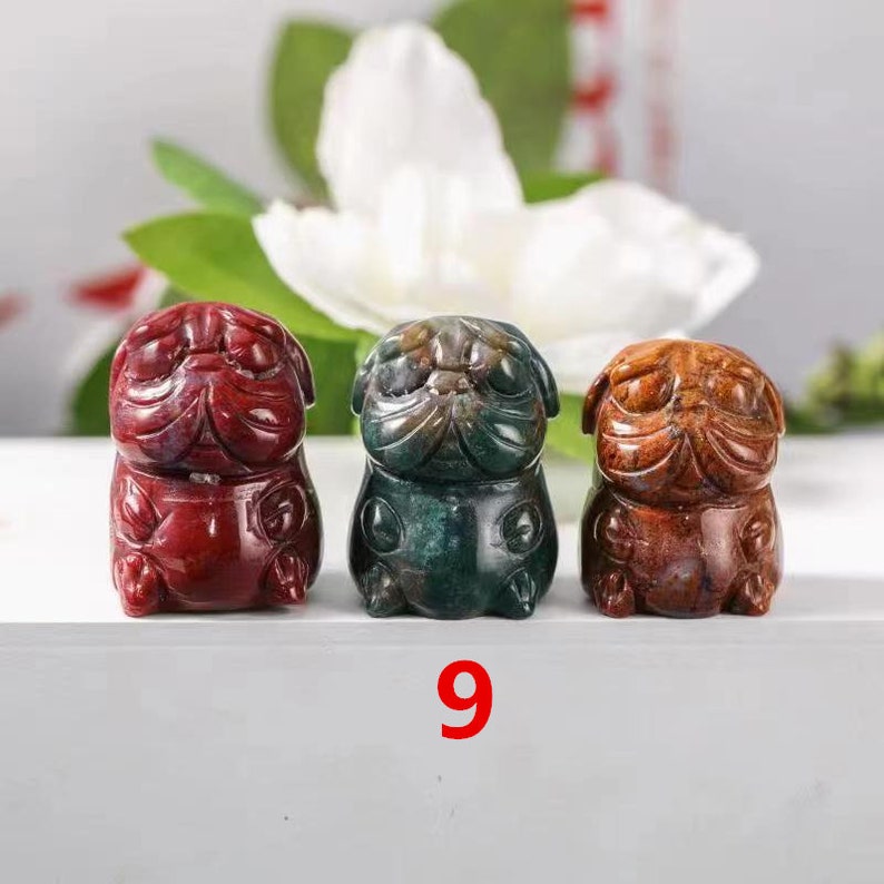 May include: Three small carved stone figurines of pugs in red, green, and brown. The figurines are sitting on a white surface with the number 9 printed below them.