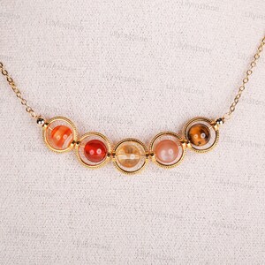May include: A gold necklace with five round gemstone beads. The beads are in shades of orange, red, and brown.