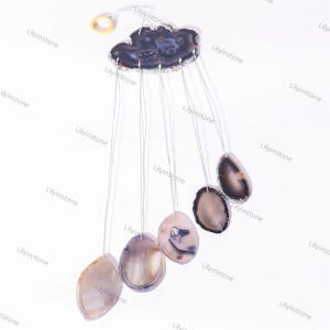 May include: A wind chime made of agate slices in shades of gray and white. The slices are suspended from a ring by thin strings. The chime is hanging from a white background.