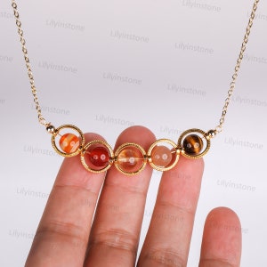 May include: A gold chain necklace with a series of six round, colorful gemstone beads. The beads are held in place by gold rings. The beads are red, orange, yellow, and brown.