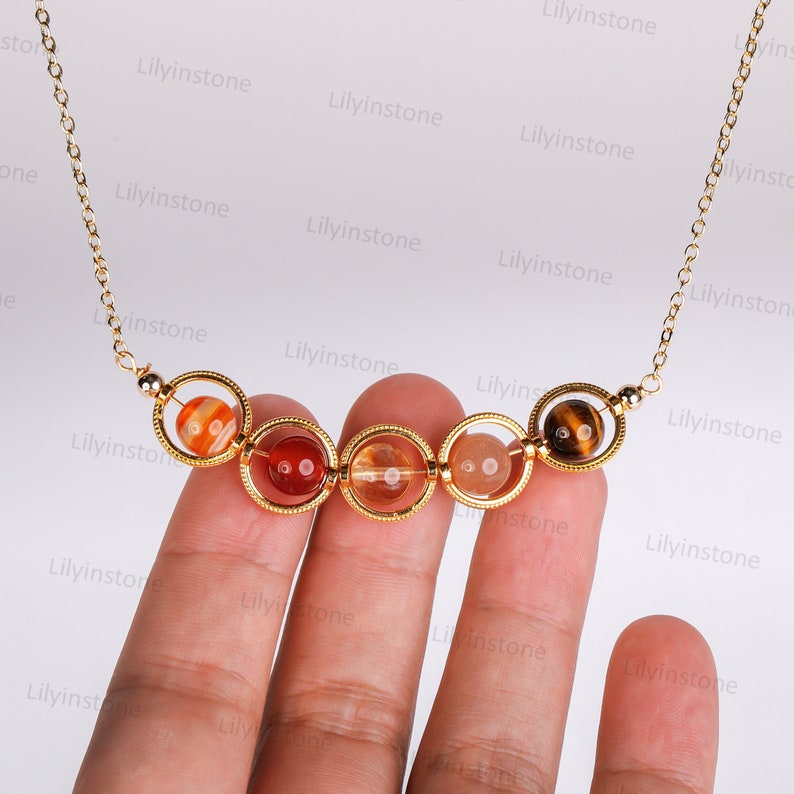 May include: A gold chain necklace with a series of six round, colorful gemstone beads. The beads are held in place by gold rings. The beads are red, orange, yellow, and brown.