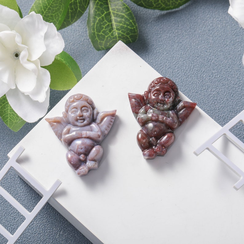 May include: Two carved cherub figurines made of red and white agate. The cherubs are sitting with their wings spread out.