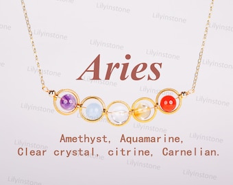May include: A gold chain necklace with a pendant featuring five gemstone beads in a circle. The beads are amethyst, aquamarine, clear crystal, citrine, and carnelian. The necklace is labeled "Aries".