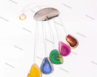 Puede incluir: Un carillón de viento hecho de rodajas de ágata en varios colores, incluyendo verde, azul, amarillo, rosa y marrón. Las rodajas están suspendidas de una rodaja de ágata gris en la parte superior.