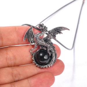 May include: A silver dragon pendant necklace with a black gemstone. The dragon is curled around the gemstone, with its wings spread out.