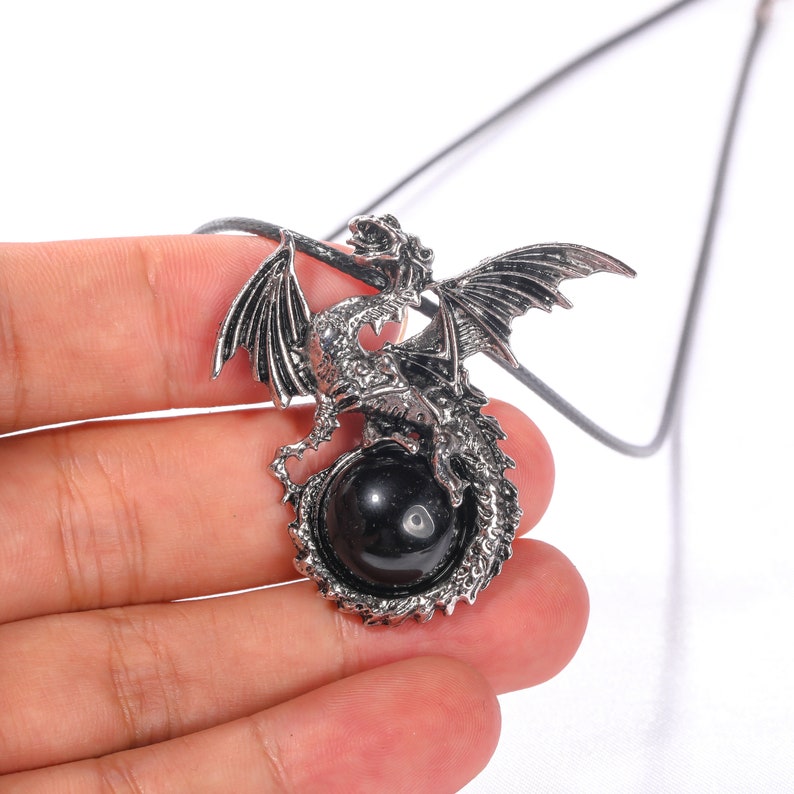 May include: A silver dragon pendant necklace with a black gemstone. The dragon is curled around the gemstone, with its wings spread out.