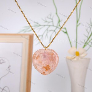 May include: A gold chain necklace with a heart-shaped pendant made of pink and orange agate.