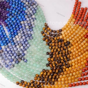 Puede incluir: Surtido de cuentas redondas de piedras preciosas en varios colores, incluyendo azul, verde, marrón, amarillo y rojo. Las cuentas están dispuestas en un patrón circular, con el texto "lilyinestone.etsy.com" visible en el centro.