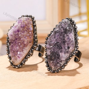 May include: Two amethyst rings with a silver-toned setting. The rings feature a large, faceted amethyst stone with a rough, natural texture. The amethyst stones are a light purple color.