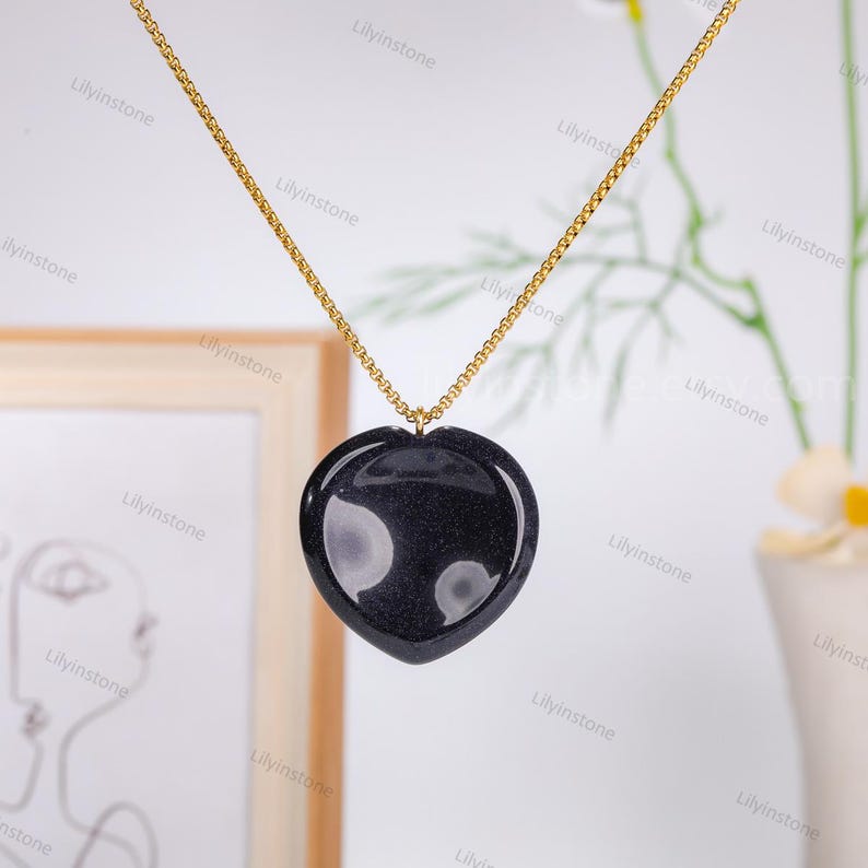May include: A gold chain necklace with a black heart-shaped pendant. The pendant has a sparkly, glittery texture.