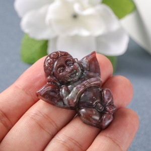May include: A red and brown agate carving of a cherub with wings, carved in a reclining pose.