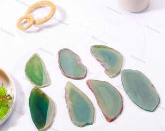 Puede incluir: Un conjunto de siete rodajas de ágata verde con diferentes tonos de verde y marrón. Las rodajas están suspendidas de un anillo de madera y una cuerda, creando un móvil o un carillón.