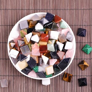 Peut inclure: Un bol blanc rempli de petites pierres pr&eacute;cieuses color&eacute;es en forme de pyramide. Le bol est pos&eacute; sur un tapis de bambou brun.