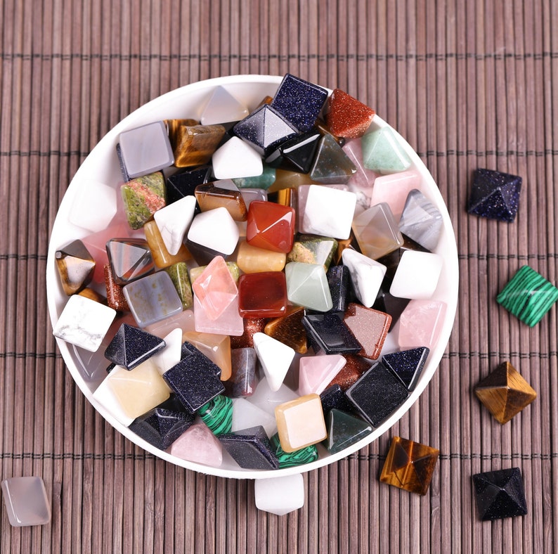 Peut inclure: Un bol blanc rempli de petites pierres pr&eacute;cieuses color&eacute;es en forme de pyramide. Le bol est pos&eacute; sur un tapis de bambou brun.