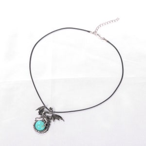May include: A black cord necklace with a silver dragon pendant featuring a turquoise gemstone.