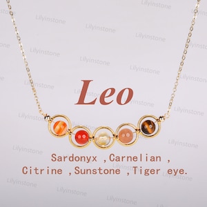 May include: Gold necklace with a charm featuring six different colored stones. The stones are labeled as Sardonyx, Carnelian, Citrine, Sunstone, and Tiger eye. The word "Leo" is written in red above the charm.