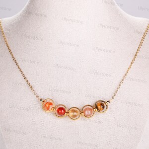 May include: A gold chain necklace with a pendant made of six round, colorful gemstones. The gemstones are set in gold circles and are arranged in a line.
