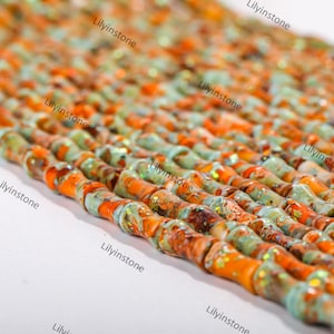 May include: A strand of orange and green gemstone beads with a glittery finish. The beads are long and cylindrical, and they are arranged in a row. The beads are all different sizes and shapes, and they have a natural, organic look.